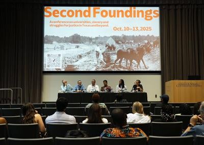 panelists in auditorium with screen text Second Foundings: A conference on universities, slavery and struggles for justice in Texas and beyond. Oct.10-13, 2025